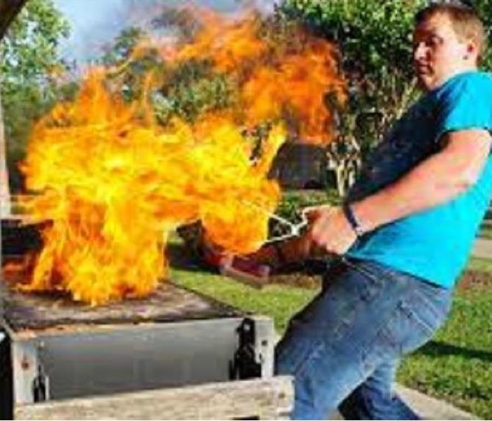 grill on fire - high flames and man stepping back from it with tongs in hand