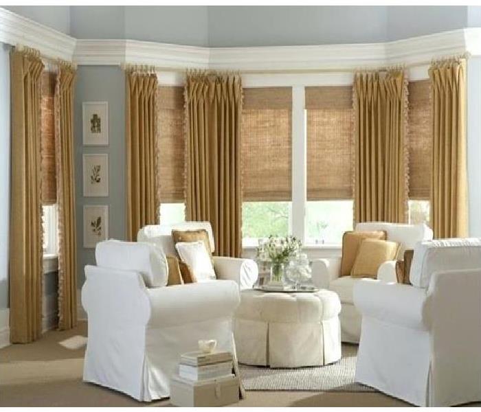 Room with white upholstered chairs with long tan drapery and cloth shades/blinds